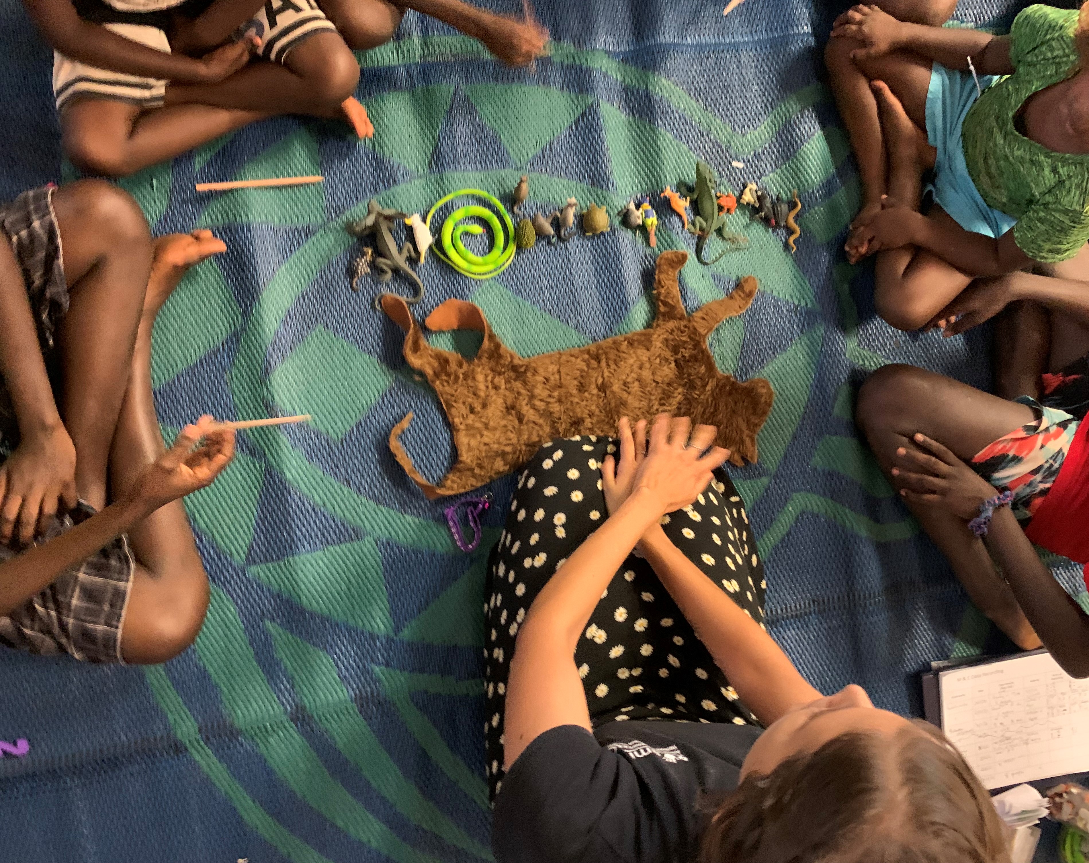 Teacher and children sitting cross-legged in front of the educational felt cat. 