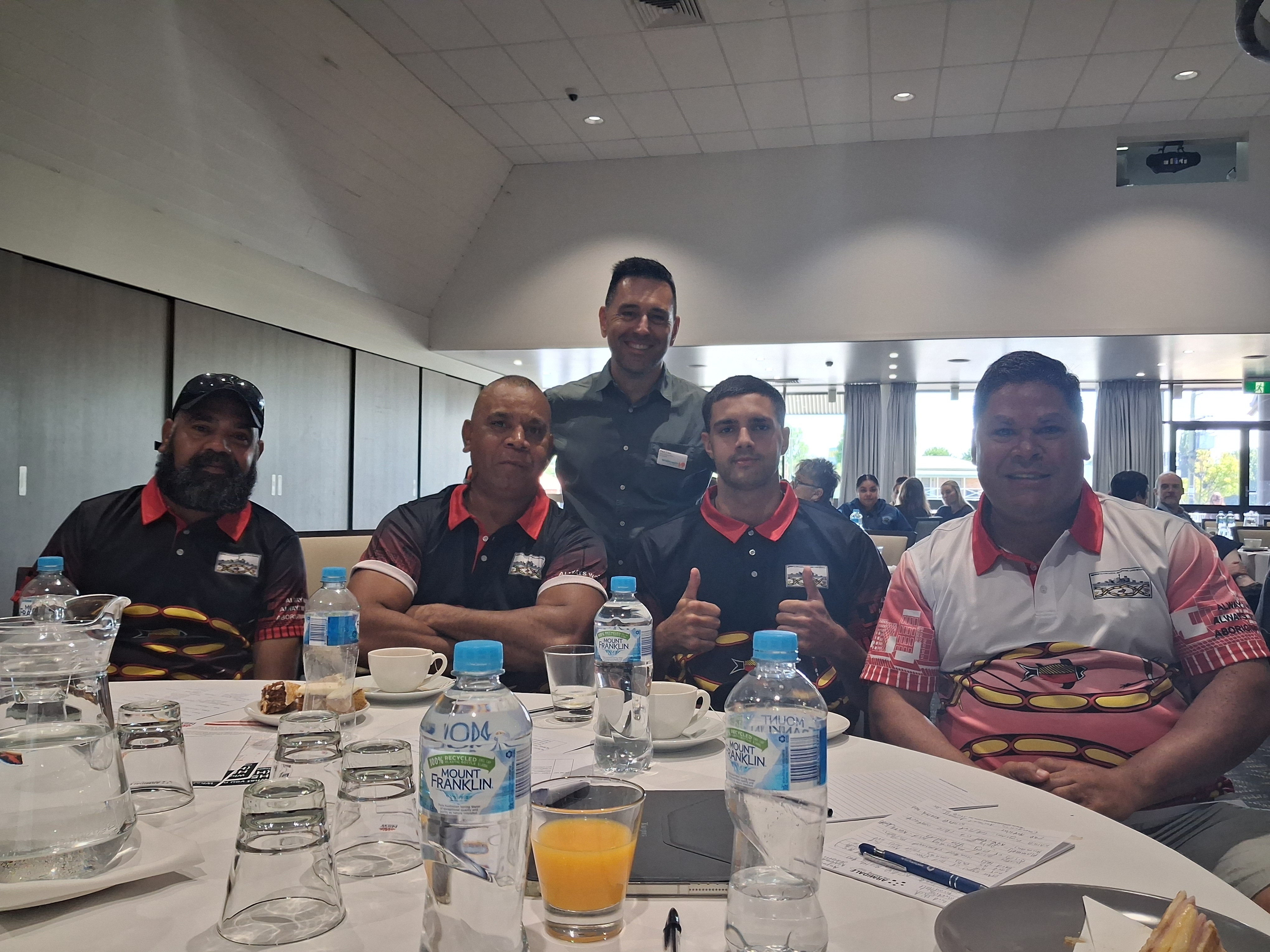 4 men sitting at a conference lunch table. Paul Eden from WHA stands behind. 